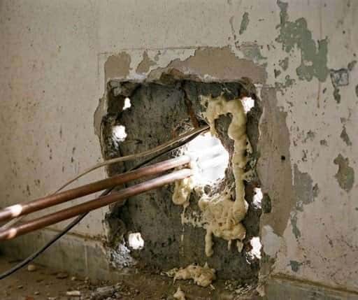 An improperly sealed AC sleeve penetration with visible gaps around the refrigerant piping. On a busy road, even a 50mm unsealed gap can undermine the acoustic performance of the entire façade