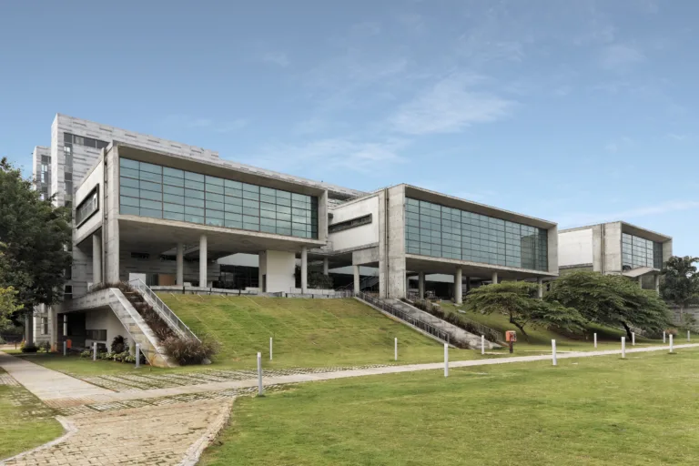 North view of the National Centre for Biological Sciences overlooking the central green maidan. The three pavilions are expressed through exposed concrete frames and large areas of structural glazing, establishing a strong relationship between the research spaces and the landscaped campus (Image Credit - ABRD)
