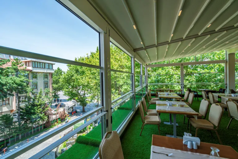 Rooftop Hospitality Space with Flexible Building Envelope - A rooftop dining terrace integrating a retractable pergola roof with vertically sliding perimeter glazing, allowing the space to transition between open-air, naturally ventilated and weather-protected configurations.